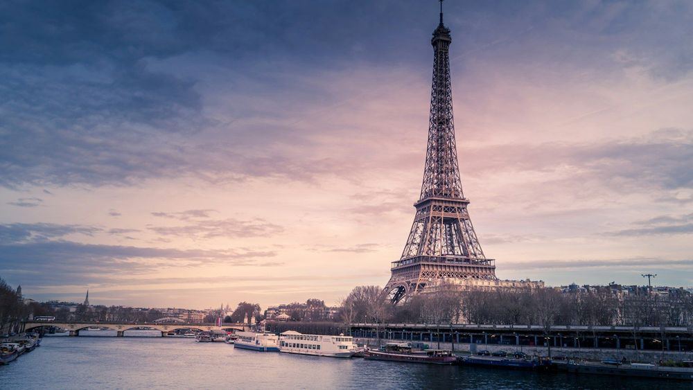 The Eiffel Tower above the Seine at dusk, with river boats moored along the bank