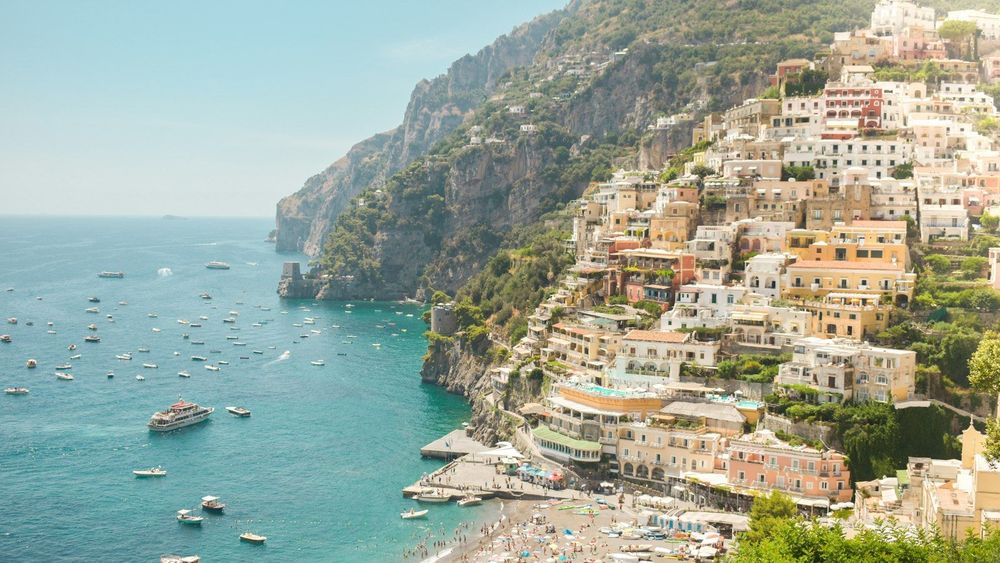 Positano's pastel houses stacked up the cliffs above a beach and boats on the Amalfi Coast