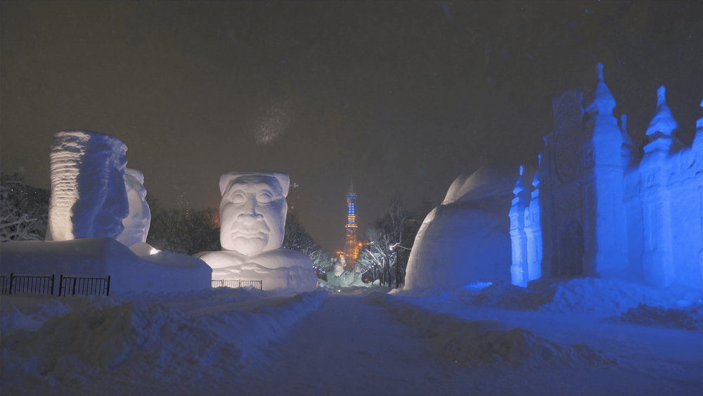 Illuminated giant snow sculptures at night at the Sapporo Snow Festival, with the TV tower in the distance