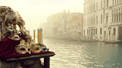 Ornate gold and white Venetian carnival masks beside a misty Grand Canal lined with palazzi and gondola poles