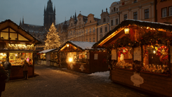 European Christmas market at dusk, with lit wooden stalls, a decorated Christmas tree, a gothic church and snow on the cobblestones