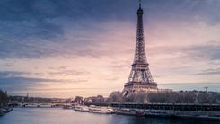 The Eiffel Tower above the Seine at dusk, with river boats moored along the bank