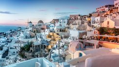 Whitewashed houses, a windmill and a Greek flag in Oia, Santorini, at dusk above the Aegean