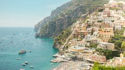 Positano's pastel houses stacked up the cliffs above a beach and boats on the Amalfi Coast