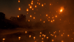 Glowing paper lanterns rising into the night sky over a river during the Yi Peng festival in Chiang Mai