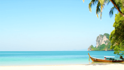 Thai longtail boat on a white sand beach with turquoise water, limestone cliffs and palm trees
